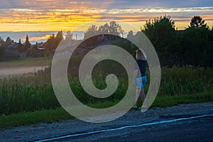 A young red-haired woman on a summer evening looks at the rural landscape. Fog over a field in the village. Shallow depth of field