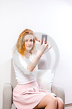 A young red-haired woman uses a mobile phone for video communication. Student on online confession on a white background. Female