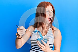 Young red head girl eating measure meter doing diet for weight loss angry and mad screaming frustrated and furious, shouting with