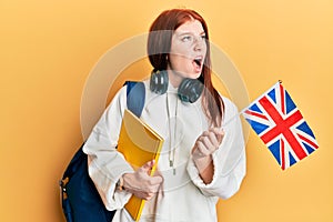 Young red head girl exchange student holding uk flag angry and mad screaming frustrated and furious, shouting with anger