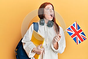 Young red head girl exchange student holding uk flag angry and mad screaming frustrated and furious, shouting with anger looking