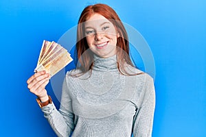 Young red head girl holding 500 norwegian krone banknotes looking positive and happy standing and smiling with a confident smile