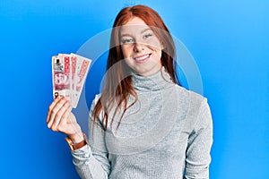 Young red head girl holding 500 swedish krona banknotes looking positive and happy standing and smiling with a confident smile