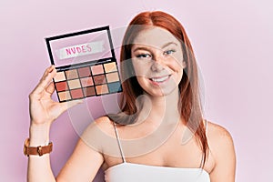 Young red head girl holding blush palette of nudes colors looking positive and happy standing and smiling with a confident smile