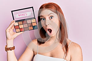 Young red head girl holding blush palette of nudes colors scared and amazed with open mouth for surprise, disbelief face
