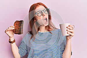 Young red head girl holding burned toast for breakfast angry and mad screaming frustrated and furious, shouting with anger looking
