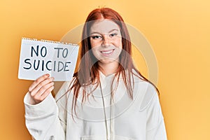 Young red head girl holding no to suicide paper looking positive and happy standing and smiling with a confident smile showing