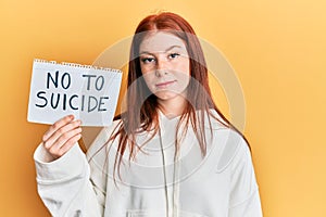 Young red head girl holding no to suicide paper thinking attitude and sober expression looking self confident