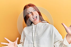 Young red head girl wearing casual sweatshirt crazy and mad shouting and yelling with aggressive expression and arms raised