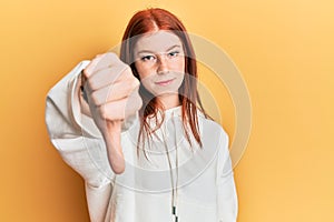 Young red head girl wearing casual sweatshirt looking unhappy and angry showing rejection and negative with thumbs down gesture