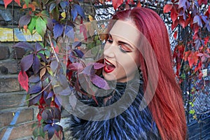 Young Red head gothic woman acting goofy and munching autumn leaves surrounded by vines