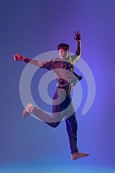 Young red-headed man, student jumping  over blue studio background in neon light. Concept of youth, fashion