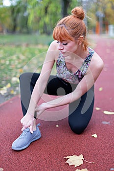 Young redhaed woman in sportswear with ankle injury on running track