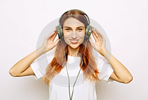 young redhair woman in basic t-shirt holding smartphone while listening to music with headphones