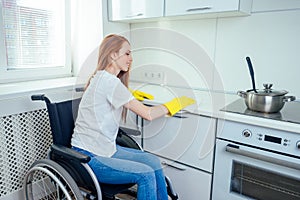 Young redhaired ginger disabled woman in wheelchair wearing yellow ribon gloves and cleaning apartment