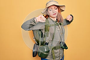 Young redhead backpacker woman hiking wearing backpack and hat over yellow background stretching back, tired and relaxed, sleepy