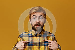 Young redhead bearded male wears checkered yellow shirt confused and amazed point with a finger on his self