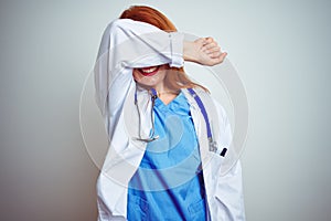 Young redhead doctor woman using stethoscope over white isolated background covering eyes with arm smiling cheerful and funny