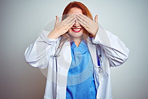 Young redhead doctor woman using stethoscope over white isolated background covering eyes with hands smiling cheerful and funny