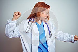 Young redhead doctor woman using stethoscope over white isolated background Dancing happy and cheerful, smiling moving casual and