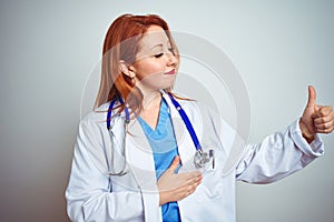 Young redhead doctor woman using stethoscope over white isolated background Looking proud, smiling doing thumbs up gesture to the