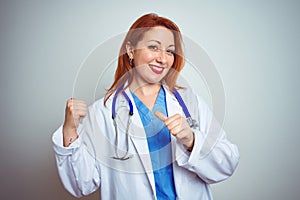 Young redhead doctor woman using stethoscope over white isolated background Pointing to the back behind with hand and thumbs up,