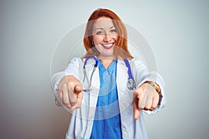 Young redhead doctor woman using stethoscope over white isolated background pointing to you and the camera with fingers, smiling