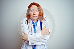 Young redhead doctor woman using stethoscope over white isolated background shaking and freezing for winter cold with sad and