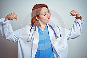 Young redhead doctor woman using stethoscope over white isolated background showing arms muscles smiling proud