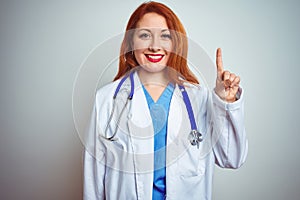 Young redhead doctor woman using stethoscope over white isolated background showing and pointing up with finger number one while