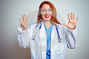Young redhead doctor woman using stethoscope over white isolated background showing and pointing up with fingers number nine while