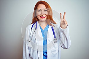 Young redhead doctor woman using stethoscope over white isolated background showing and pointing up with fingers number two while
