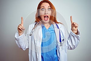 Young redhead doctor woman using stethoscope over white isolated background smiling amazed and surprised and pointing up with