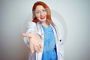 Young redhead doctor woman using stethoscope over white isolated background smiling cheerful offering palm hand giving assistance