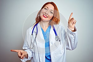 Young redhead doctor woman using stethoscope over white isolated background smiling confident pointing with fingers to different