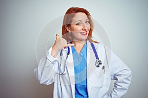 Young redhead doctor woman using stethoscope over white isolated background smiling doing phone gesture with hand and fingers like