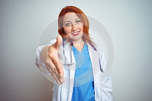 Young redhead doctor woman using stethoscope over white isolated background smiling friendly offering handshake as greeting and