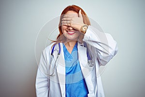 Young redhead doctor woman using stethoscope over white isolated background smiling and laughing with hand on face covering eyes