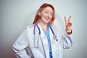 Young redhead doctor woman using stethoscope over white isolated background smiling looking to the camera showing fingers doing