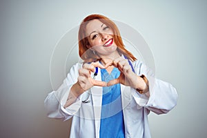 Young redhead doctor woman using stethoscope over white isolated background smiling in love doing heart symbol shape with hands