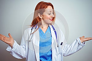 Young redhead doctor woman using stethoscope over white isolated background smiling showing both hands open palms, presenting and