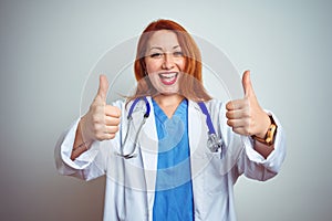 Young redhead doctor woman using stethoscope over white isolated background success sign doing positive gesture with hand, thumbs