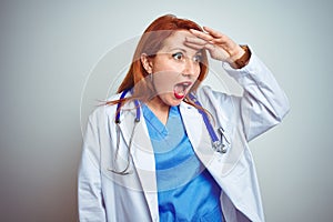 Young redhead doctor woman using stethoscope over white isolated background very happy and smiling looking far away with hand over