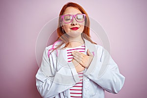 Young redhead doctor woman using stethoscope standing over isolated pink background smiling with hands on chest with closed eyes