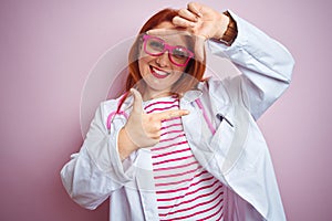 Young redhead doctor woman using stethoscope standing over isolated pink background smiling making frame with hands and fingers