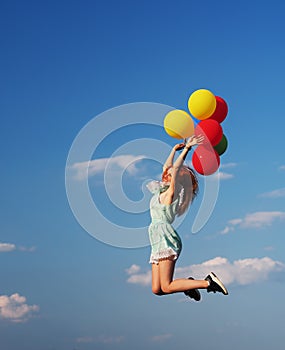 Young redhead girl with colorful balloons jumping at the blue sky