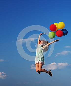 Young redhead girl with colorful balloons jumping at the blue sky