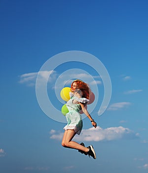Young redhead girl with colorful balloons jumping at the blue sky