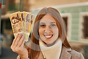 Young redhead girl smiling happy holding hungarian forint banknotes at the city