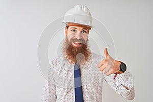 Young redhead irish architect man wearing security helmet over isolated white background doing happy thumbs up gesture with hand